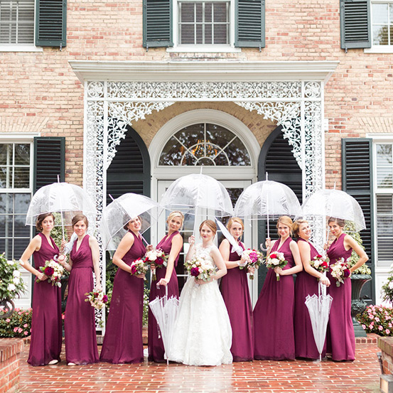 Bride and bridesmaids holding umbrellas outside during inclement weather