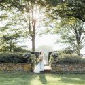 Bride along stone in garden holding large bridal bouquet