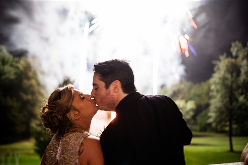 Bride and groom kissing with fireworks going off in background 
