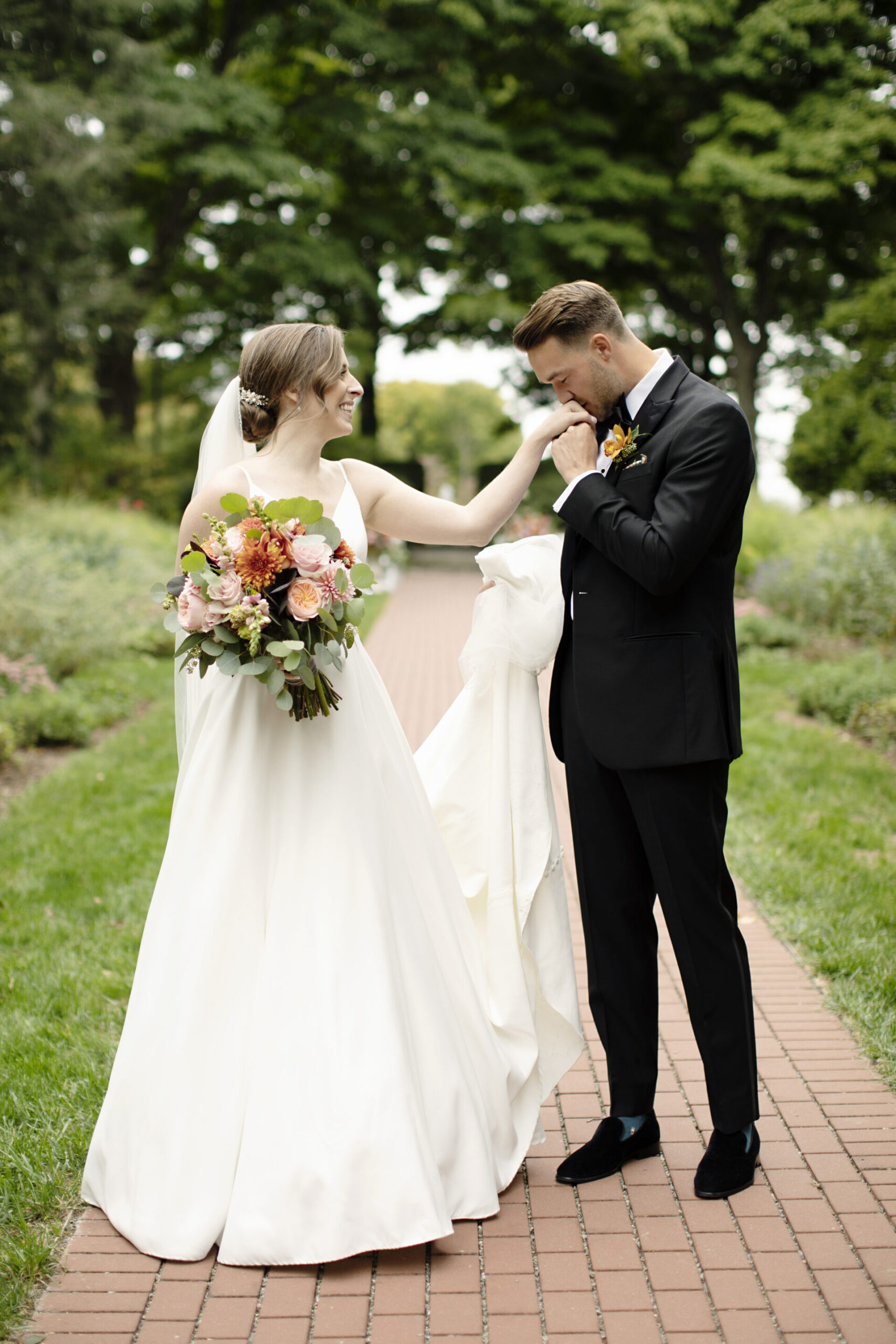 groom kissing brides hand in garden 